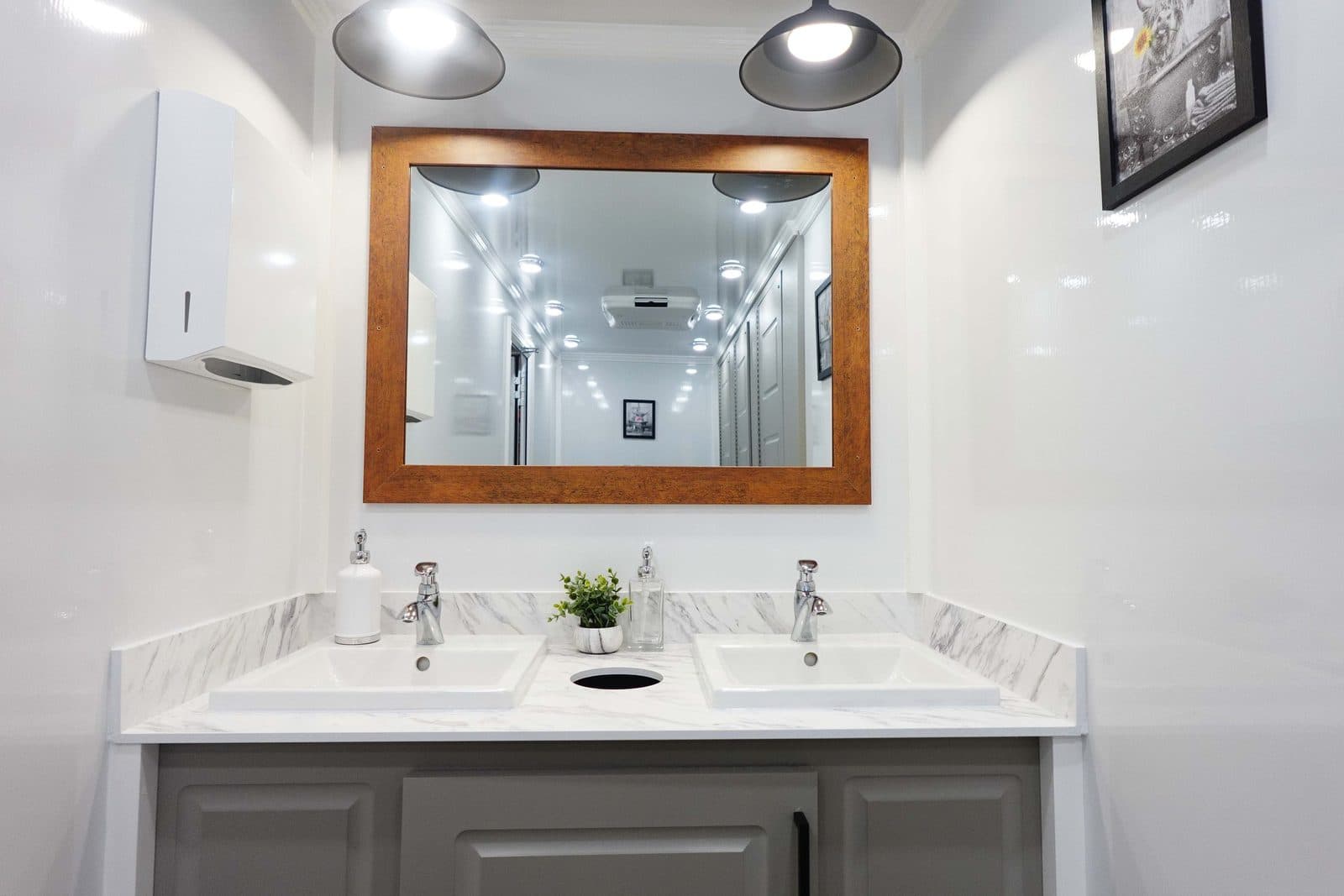 Interior of a luxury restroom trailer showing a marble-look double vanity, framed mirror, and pendant lighting