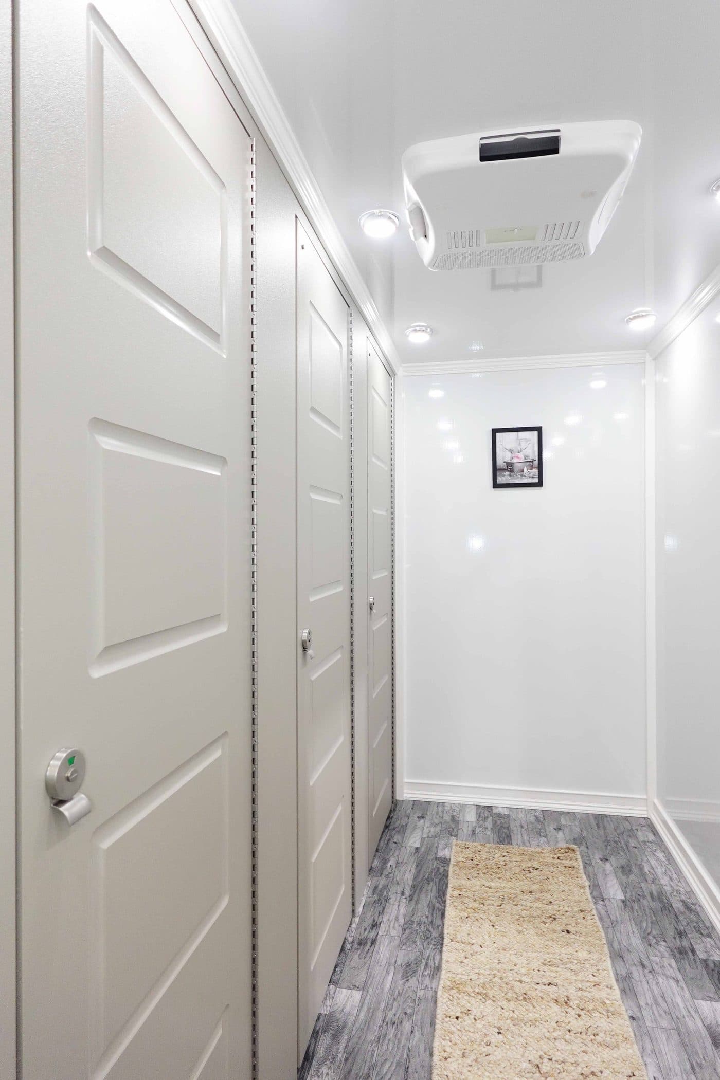 Bright interior corridor of a luxury restroom trailer with private stall doors, crown molding, and air conditioning