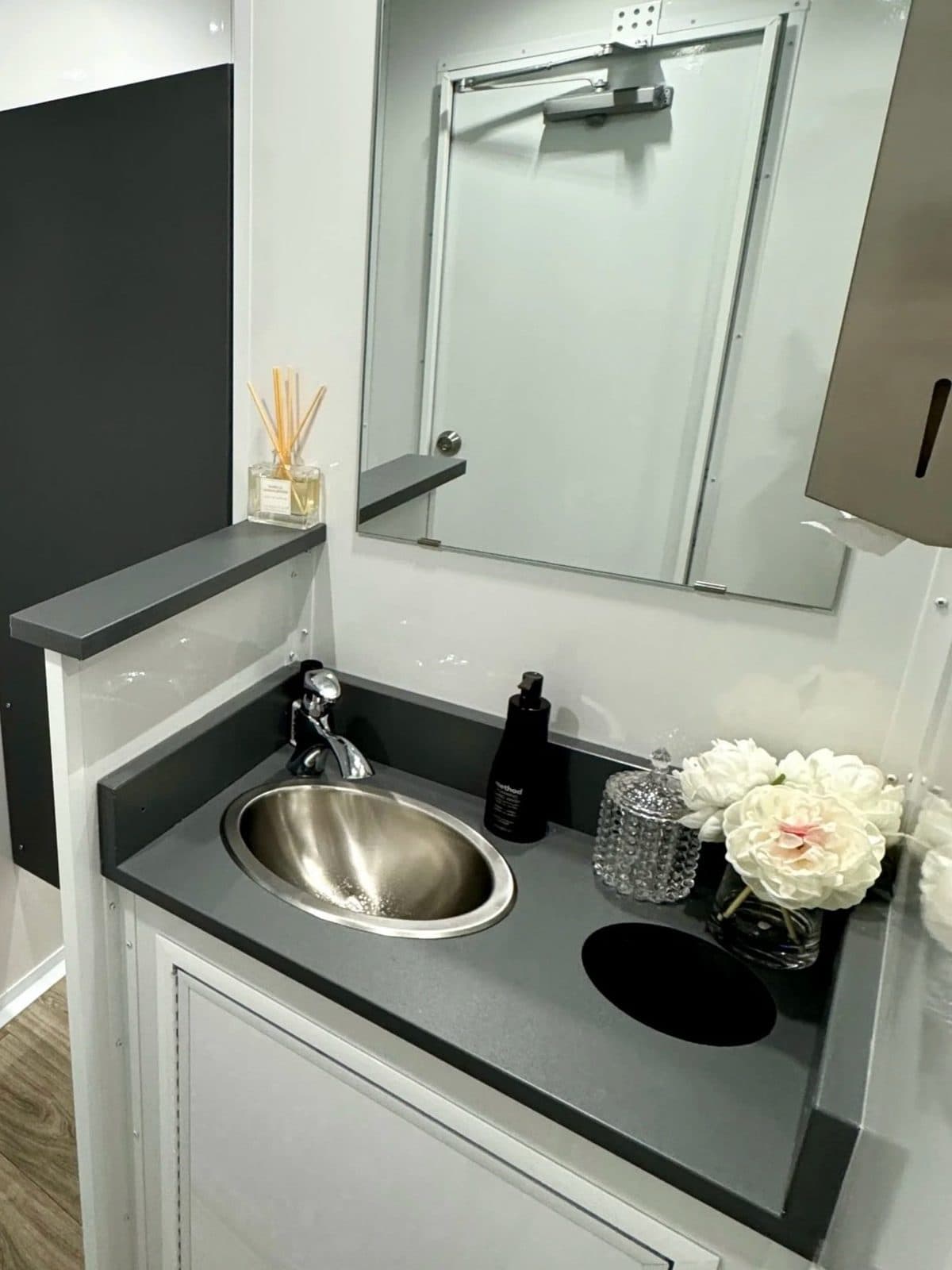 Stainless steel sink and mirror detail inside a luxury restroom trailer with fresh flowers