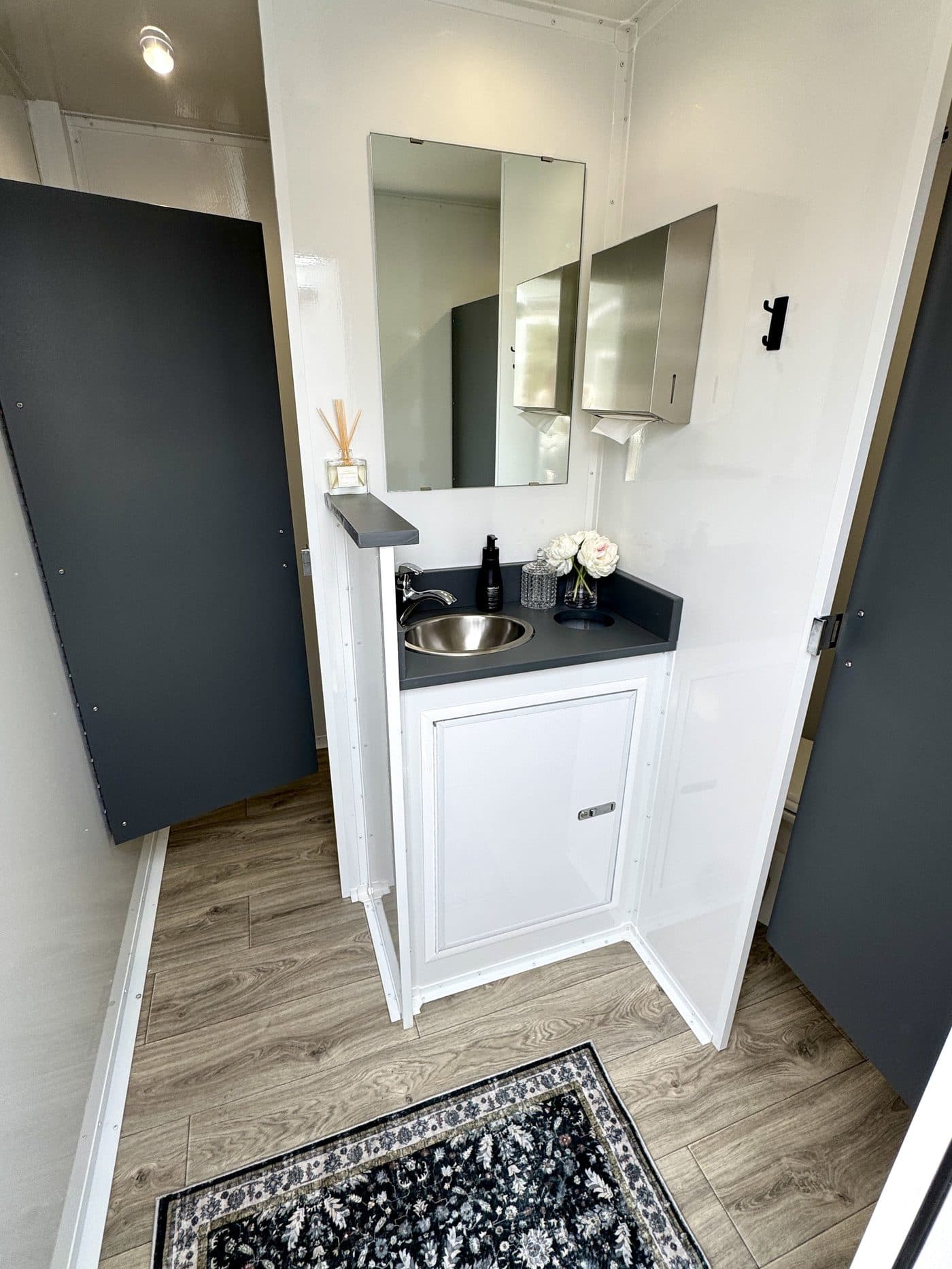 Vanity inside a luxury restroom trailer styled with fresh flowers, hand soap, and a lit mirror